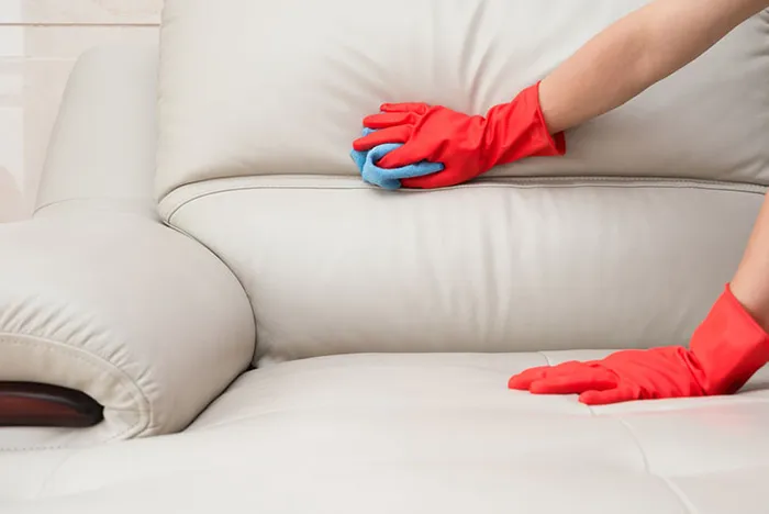 A person in red gloves meticulously cleaning a white couch,
